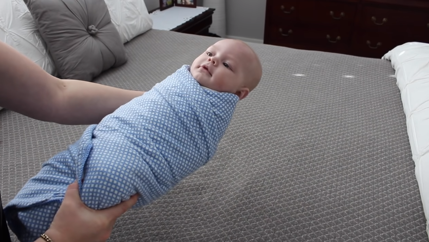 newborn using a blue dotted swaddle 