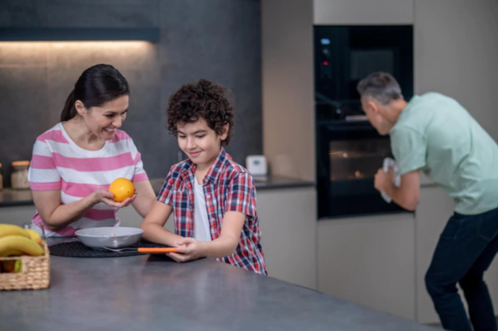Boy with tablet and parents behind cooking in kitchen